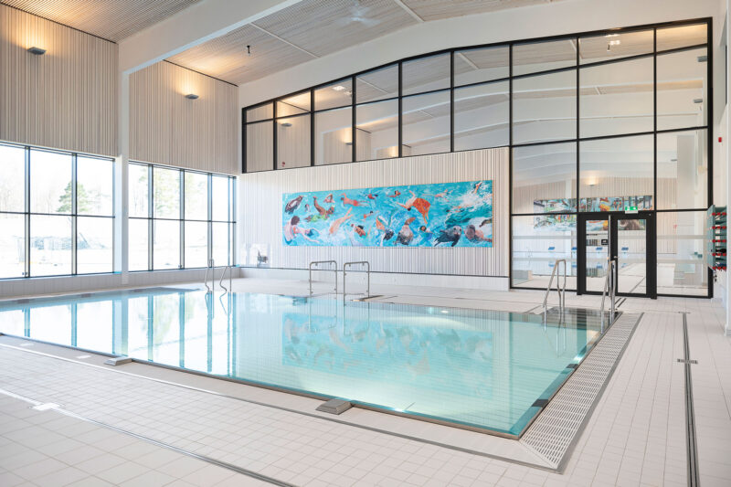 Modern indoor swimming pool with large windows and colorful artwork on the far wall.