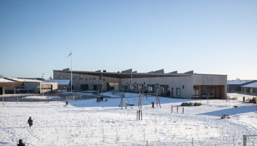 Modern wooden building with large windows surrounded by snow, children playing in the open area.