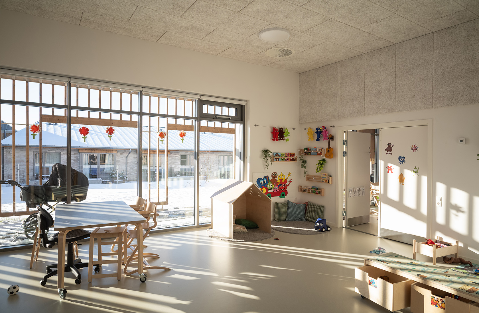 Bright children's playroom with colorful wall decorations, toys, and large windows showing a snowy scene.