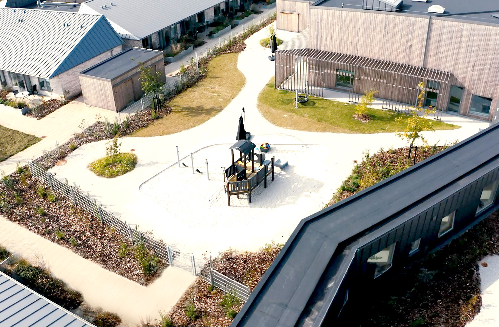 Aerial view of modern daycare center with playground surrounded by buildings and landscaped paths.