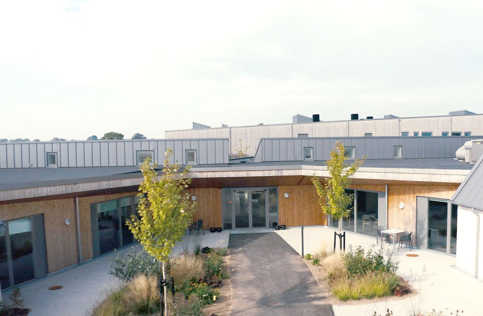 Modern architecture building with wooden and metal facade, surrounded by greenery and outdoor seating area.