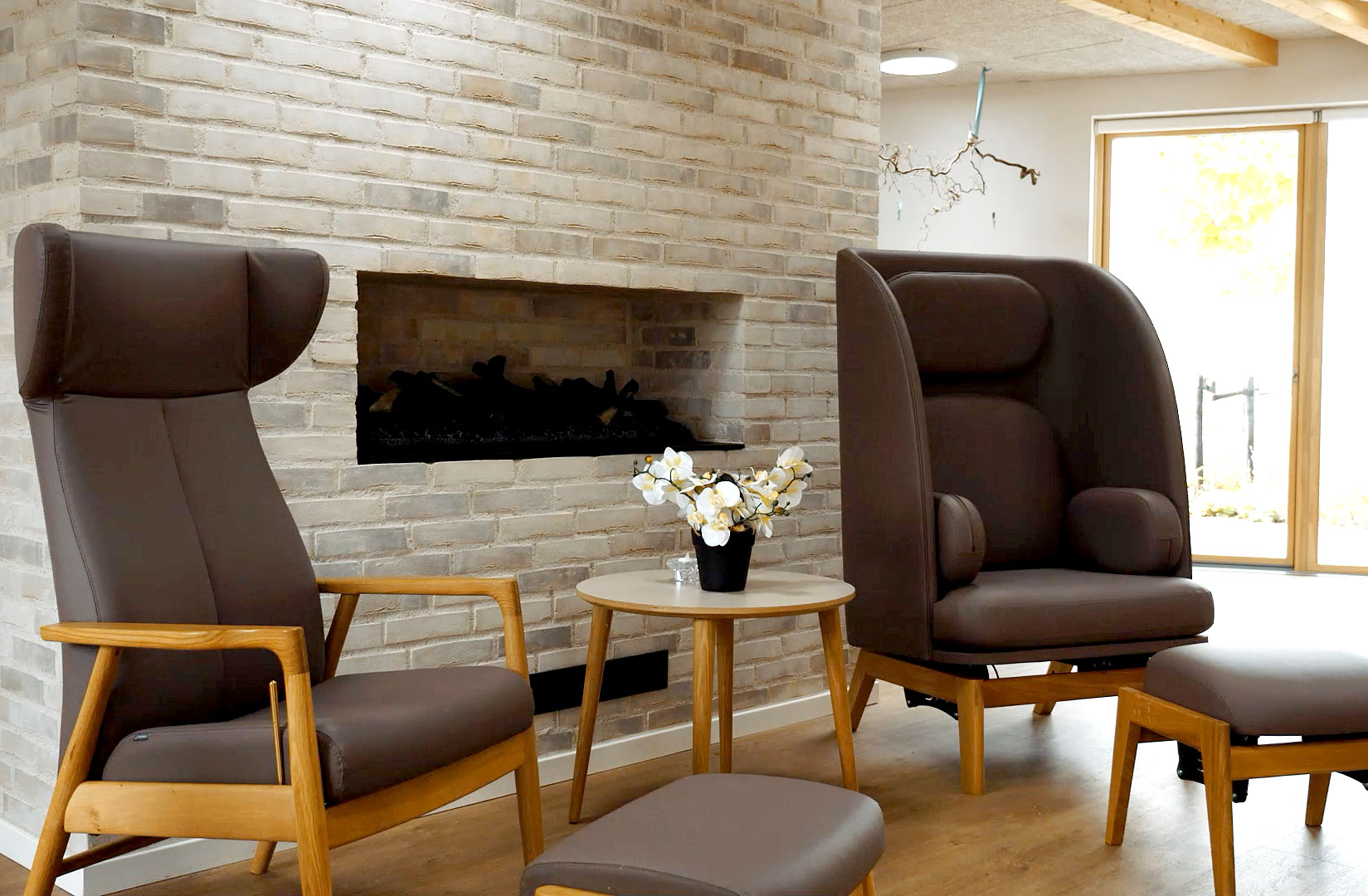 Modern living room with two brown armchairs, a fireplace, and a small table with a flower pot.