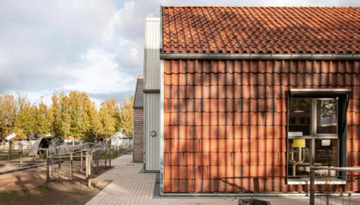 Modern daycare building with red tile facade and rural yard under cloudy sky