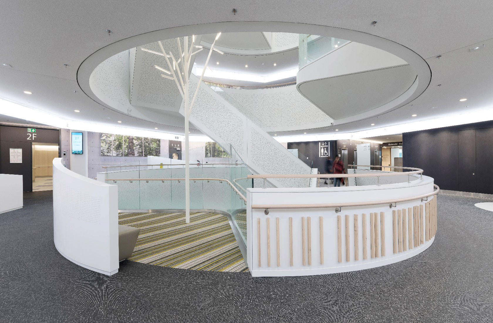 Modern hospital atrium with spiral staircase, curved railings, and bright open lobby interior