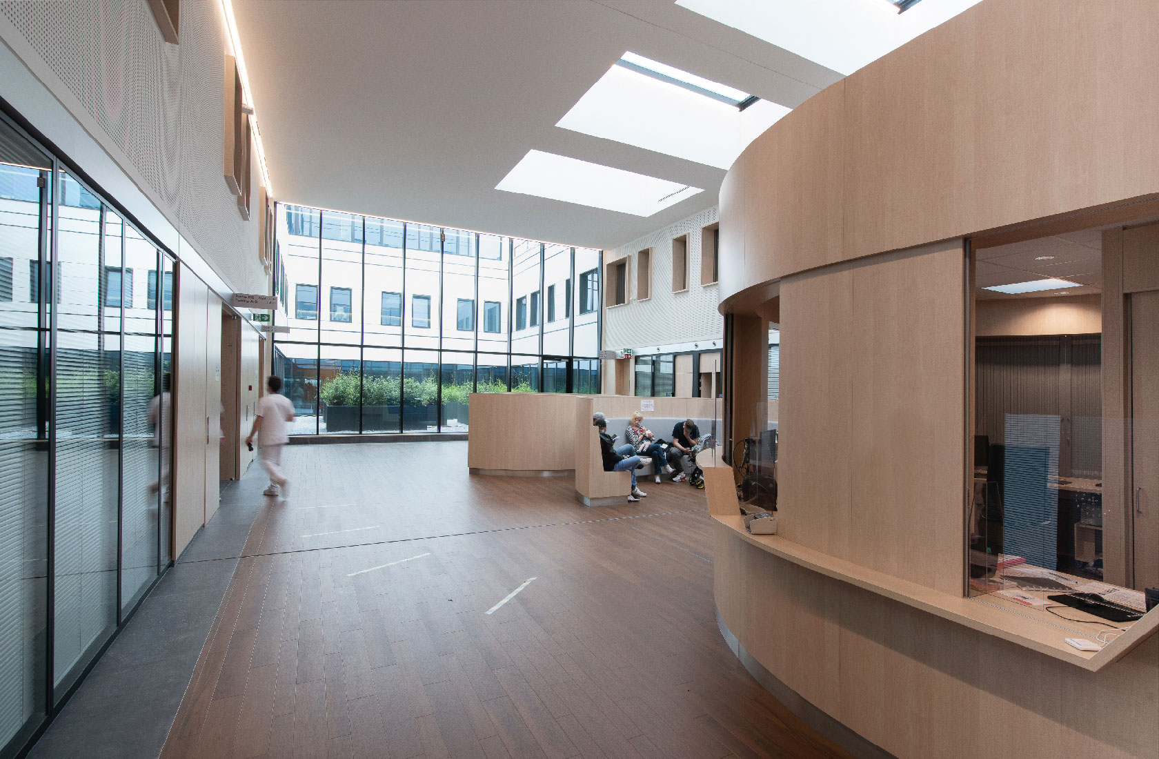 Modern hospital lobby with reception desk, waiting area, and large skylight windows