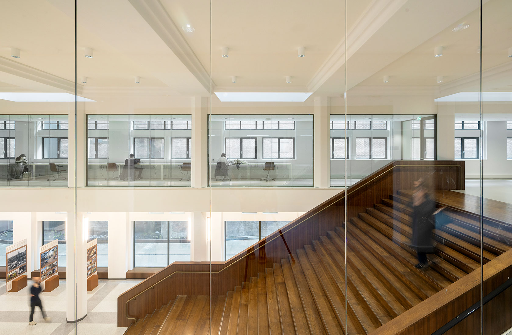 Modern university atrium with wooden staircase, glass walls, and students working at desks