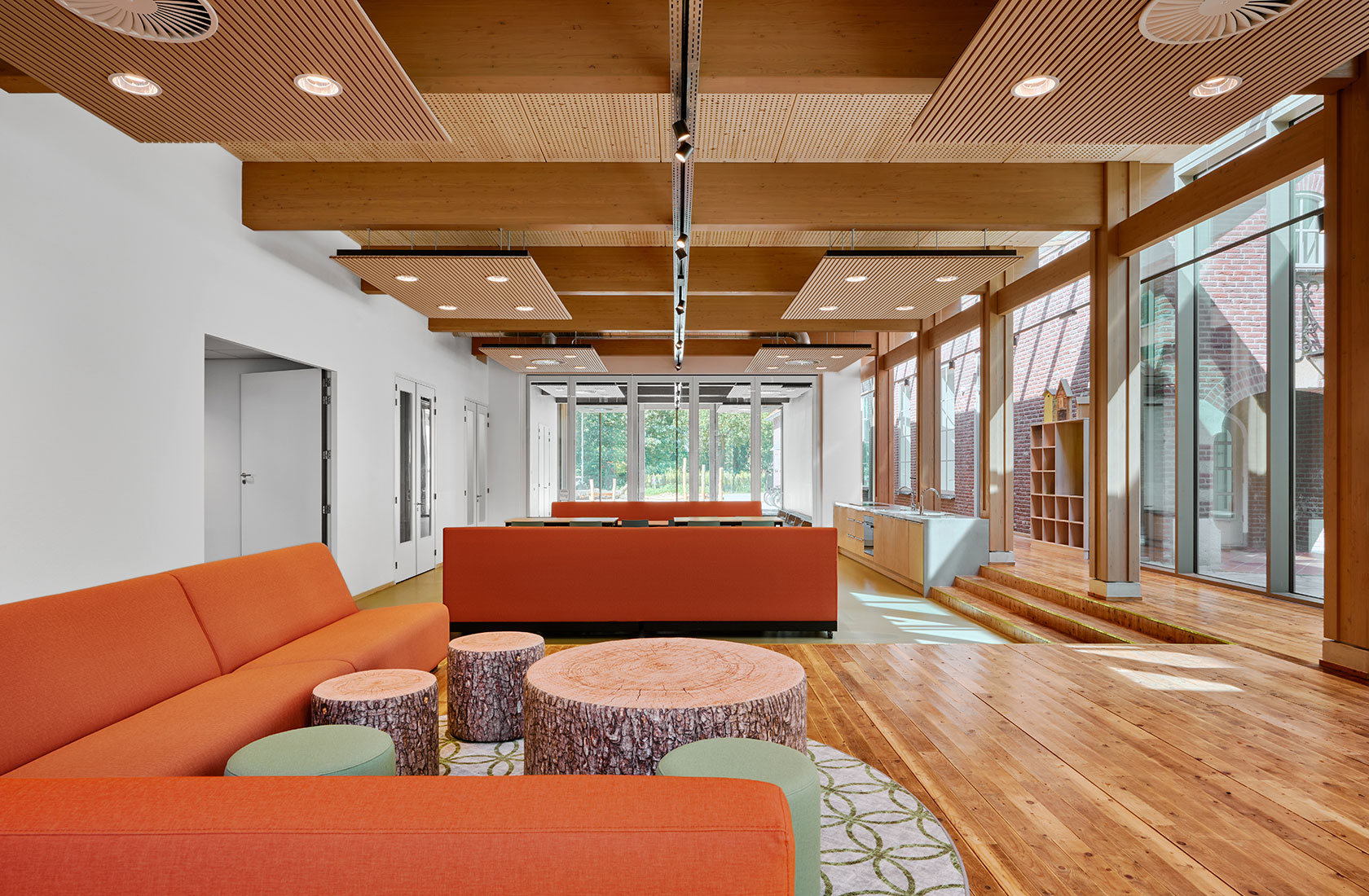 Modern lounge interior with orange sofas, wood beams, and large windows with sunlight