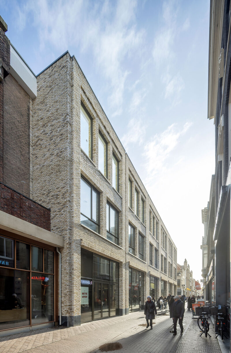 Modern brick university building on a narrow city street with pedestrians and bicycles