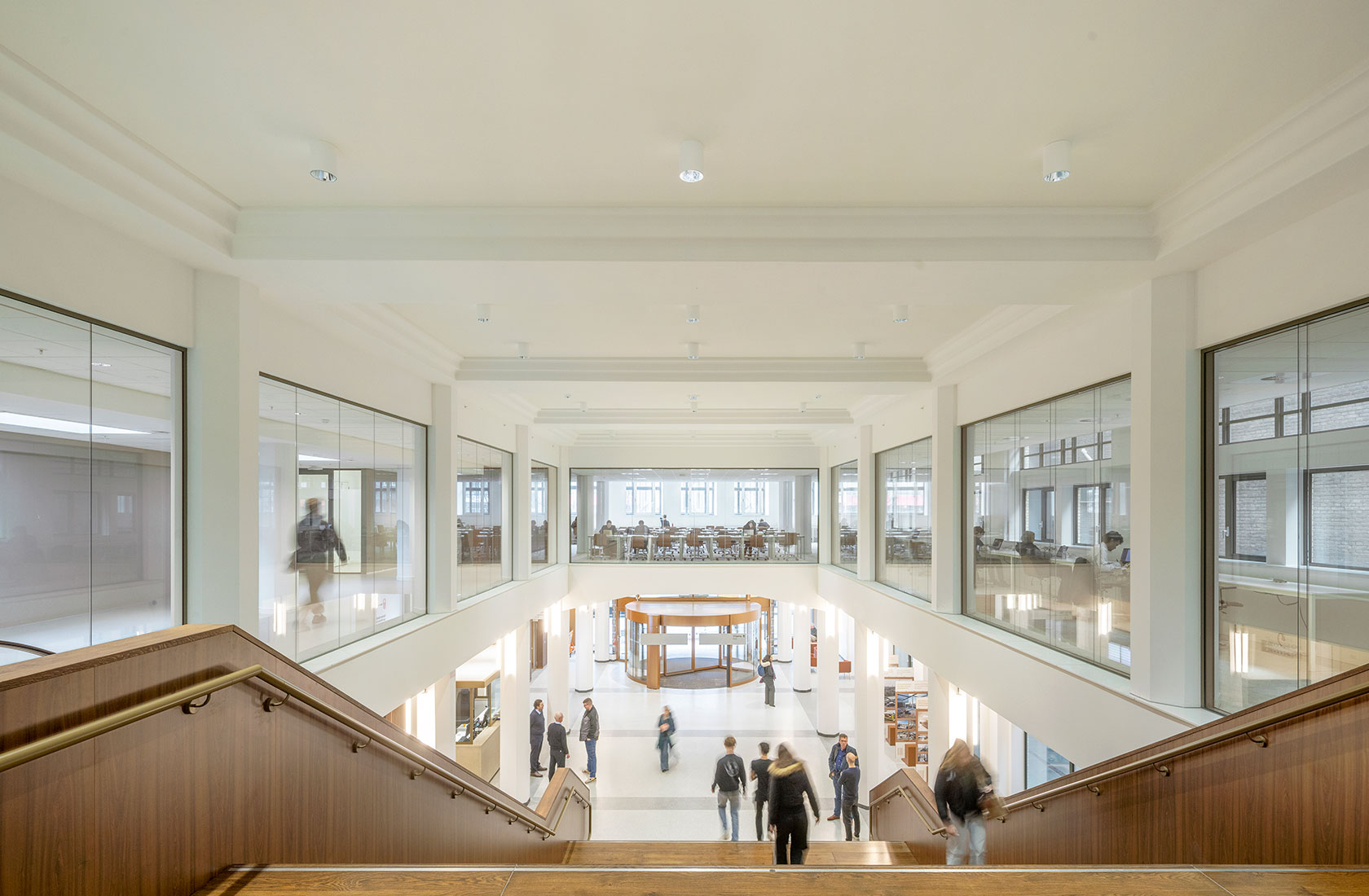 Modern university library atrium with stairs, glass study rooms, and students walking