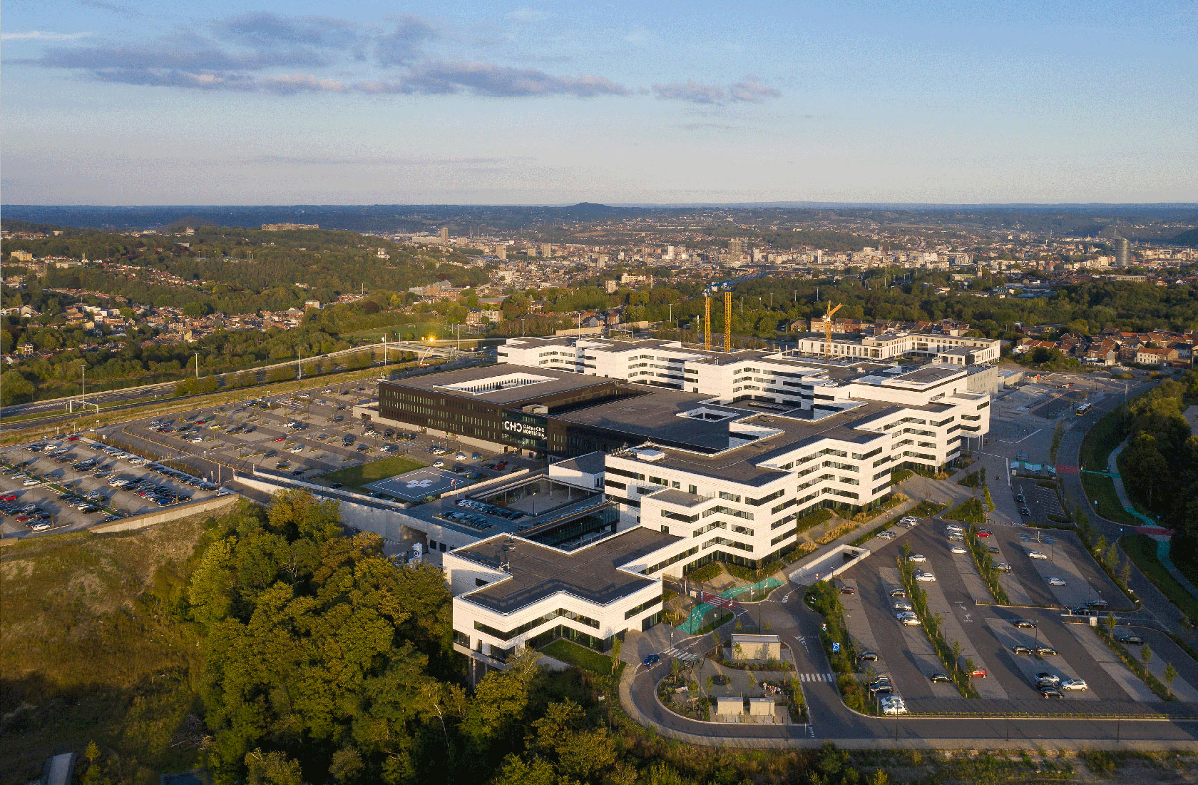 Aerial view of modern hospital complex with parking lots and city skyline at sunset