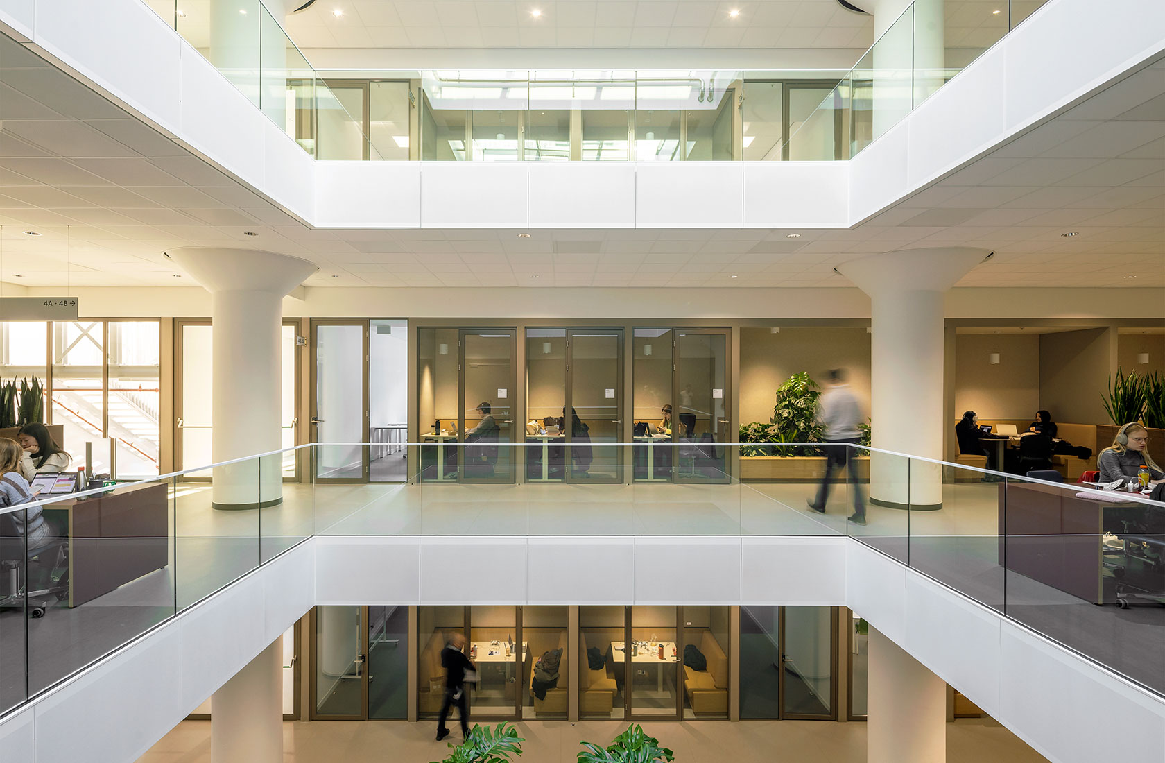 Modern university atrium with glass railings, meeting rooms, and people working