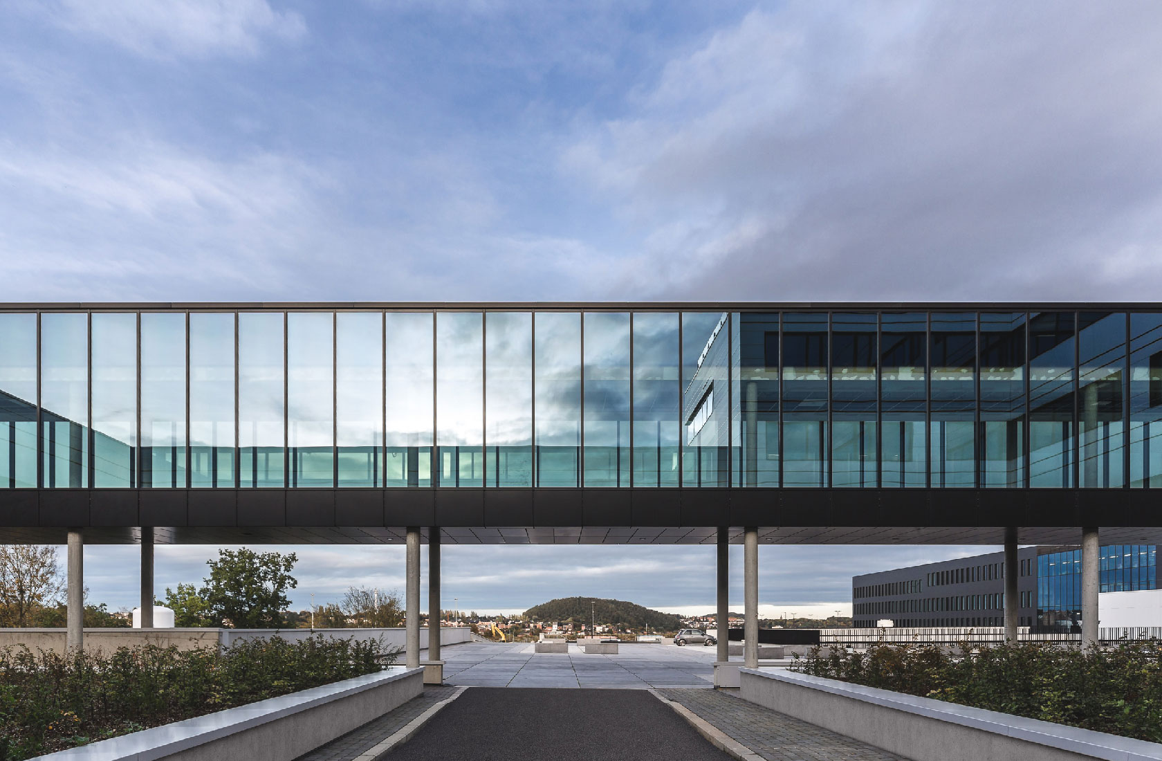 Modern glass skybridge connecting hospital buildings under cloudy blue sky