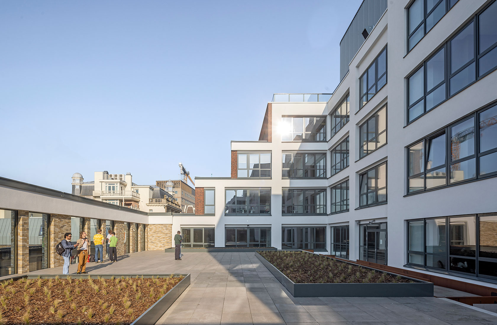 Modern university courtyard with white building facade, large windows, and rooftop terrace