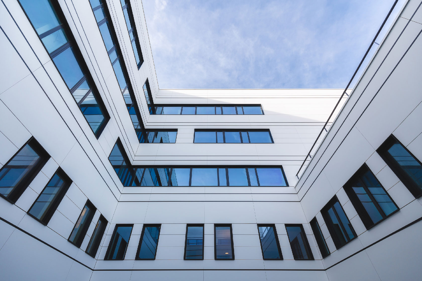 Modern hospital building courtyard with blue glass windows and white facade, upward view