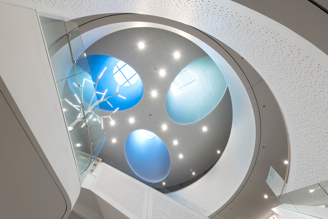 Modern circular atrium ceiling with blue skylights, recessed lights, and glass railing