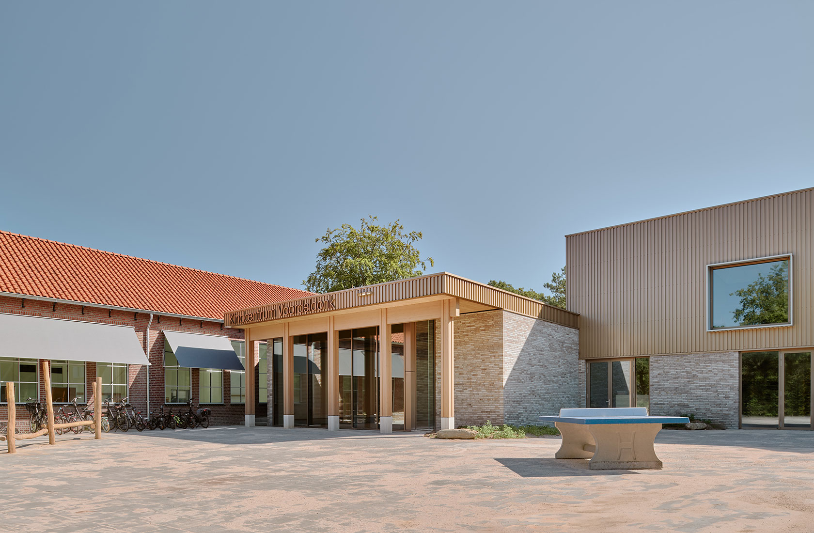 Modern school courtyard with brick and wood building entrance under clear blue sky