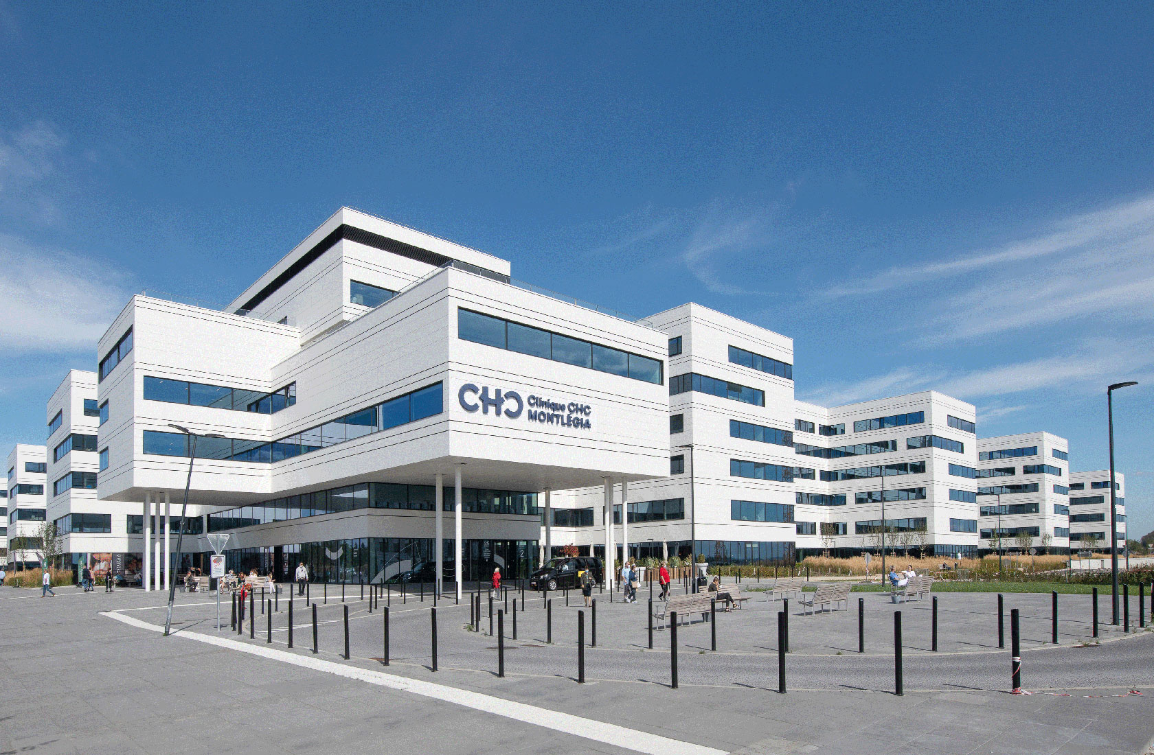 Modern hospital building exterior with blue sky and entrance plaza pedestrians