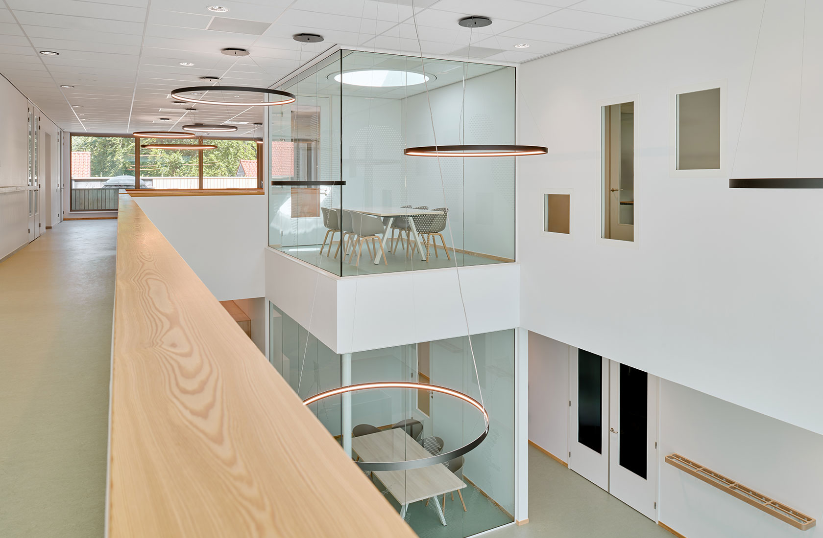 Modern school building interior with glass meeting rooms, ring pendant lights, and wood railing