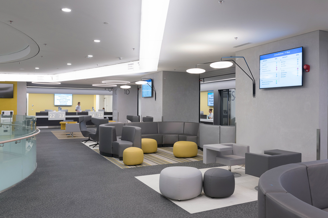 Modern hospital waiting room with seating, consultation desks, and digital information screens