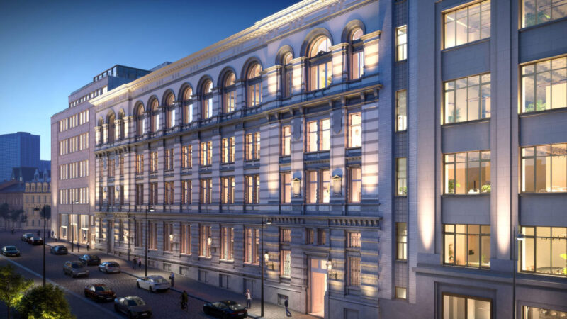 Illuminated historic office building facade on city street at dusk with cars and pedestrians