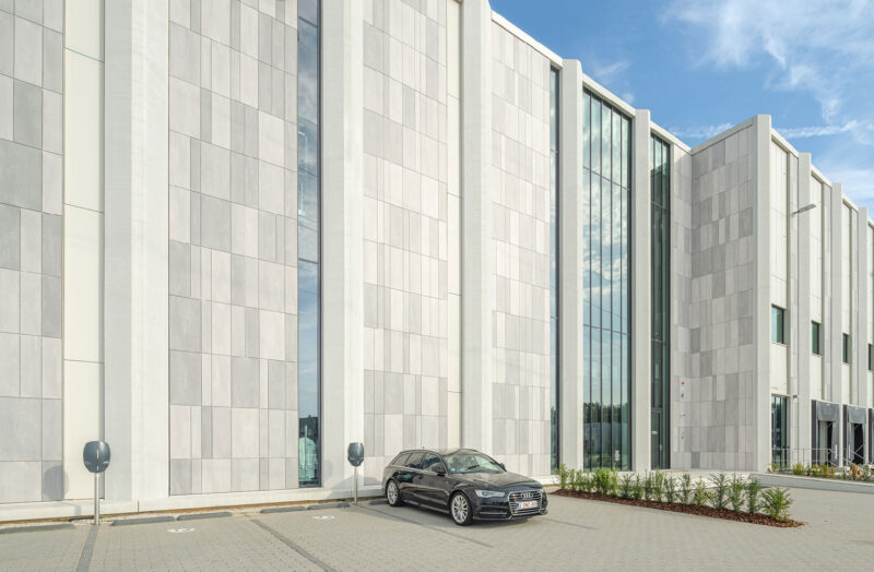 Modern industrial building facade with tall glass windows and a parked black sedan.