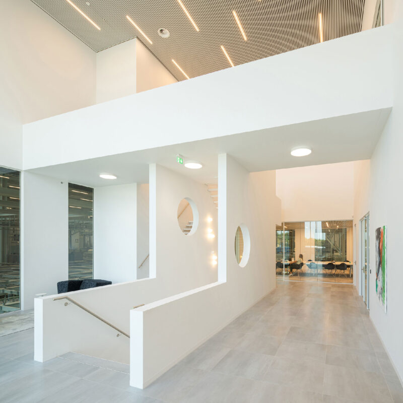 Modern office lobby interior with white walls, circular windows, and meeting room view.