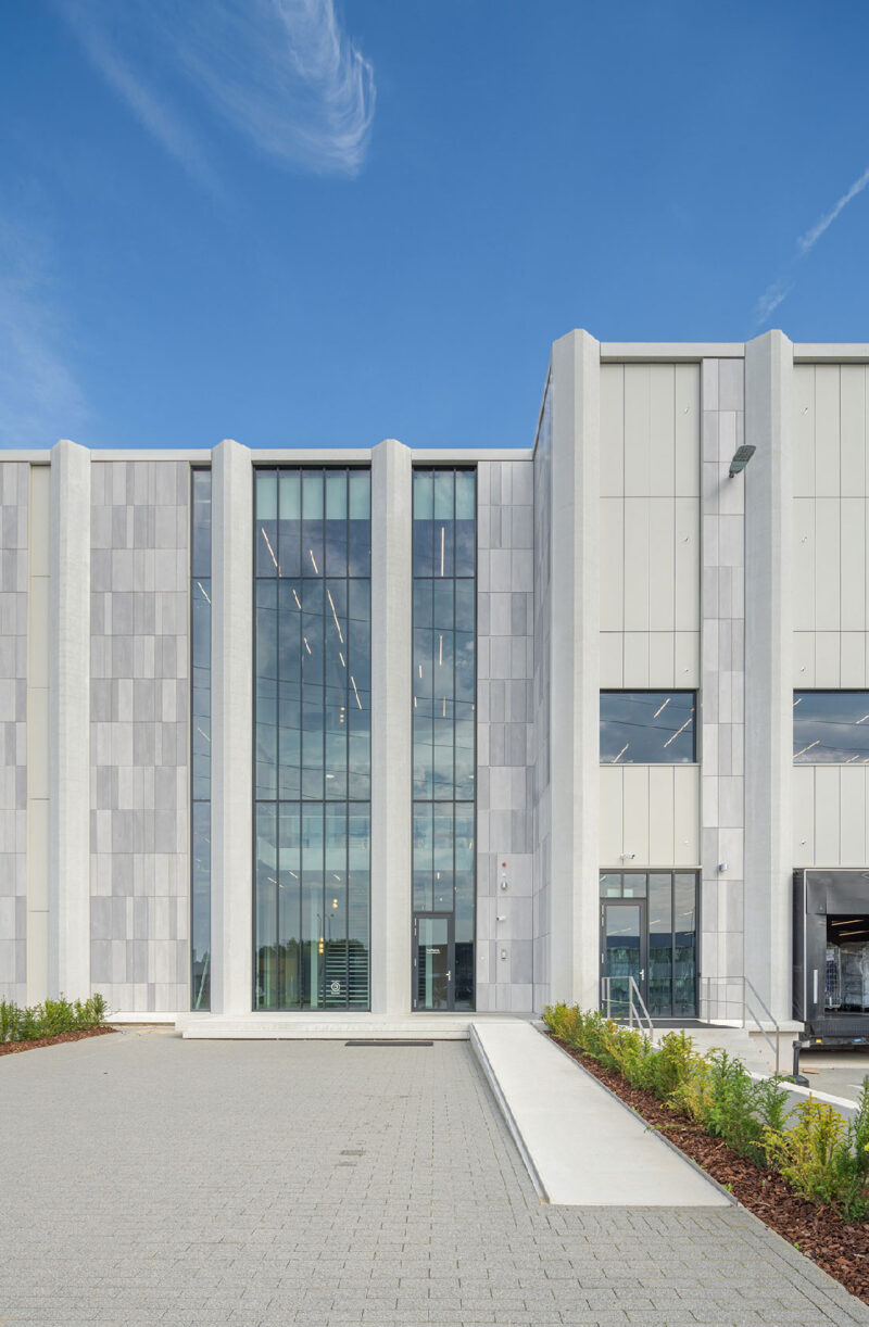 Modern industrial warehouse entrance with glass facade and loading dock under blue sky.