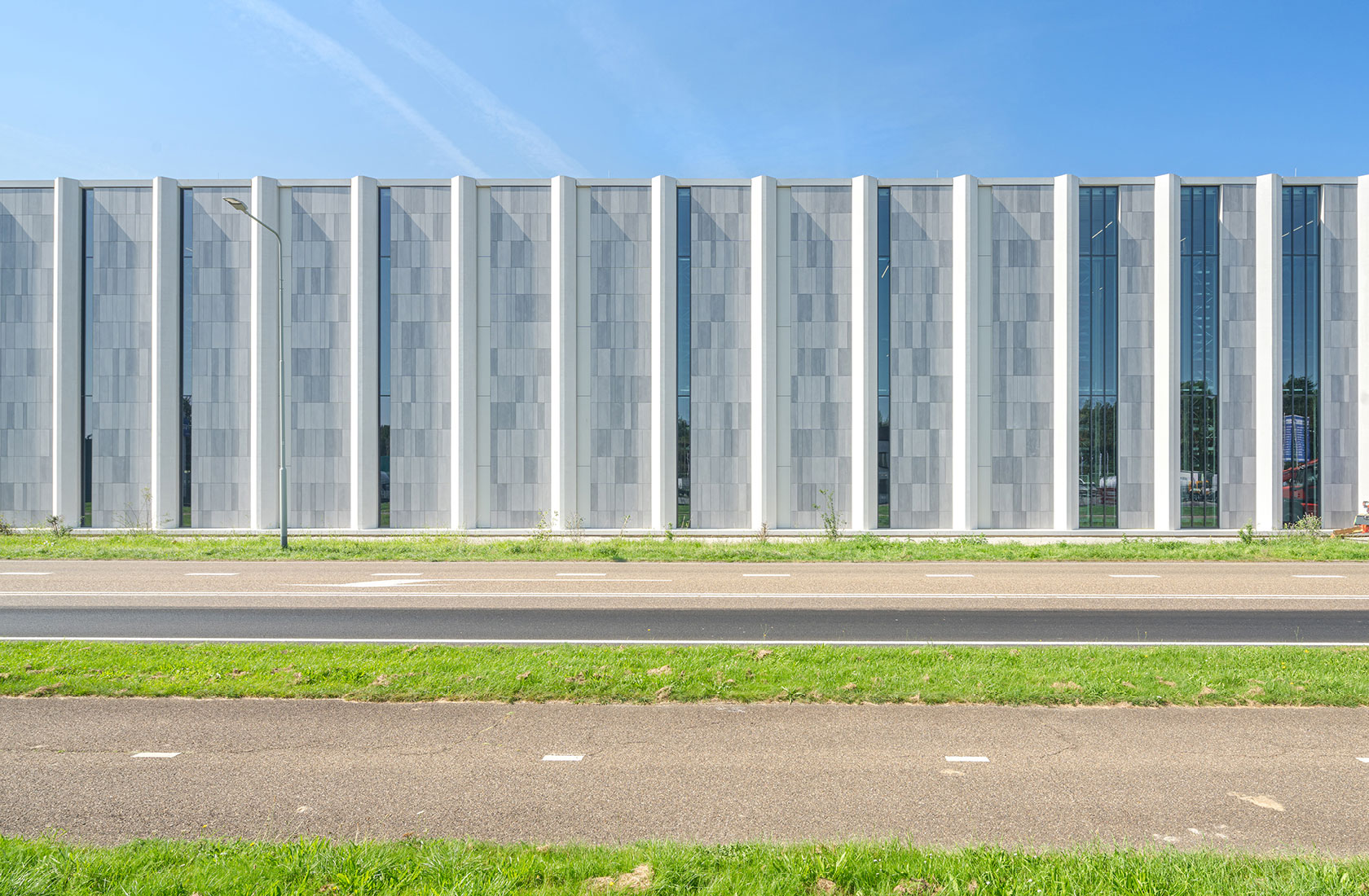 Modern white industrial building facade with tall vertical windows under blue sky.